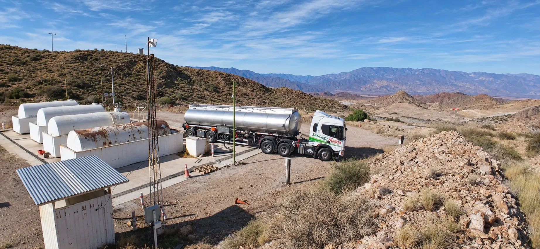Tractor de Transporte Sanchez Huerta con semirremolque cisterna de acero inoxidable descargando combustible en los tanques de una operación minera, entre cerros áridos