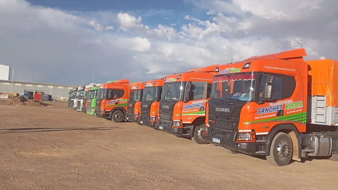 Fila de tractores Scania naranja de la flota de Transporte Sanchez Huerta estacionados en diagonal en un predio de tierra
