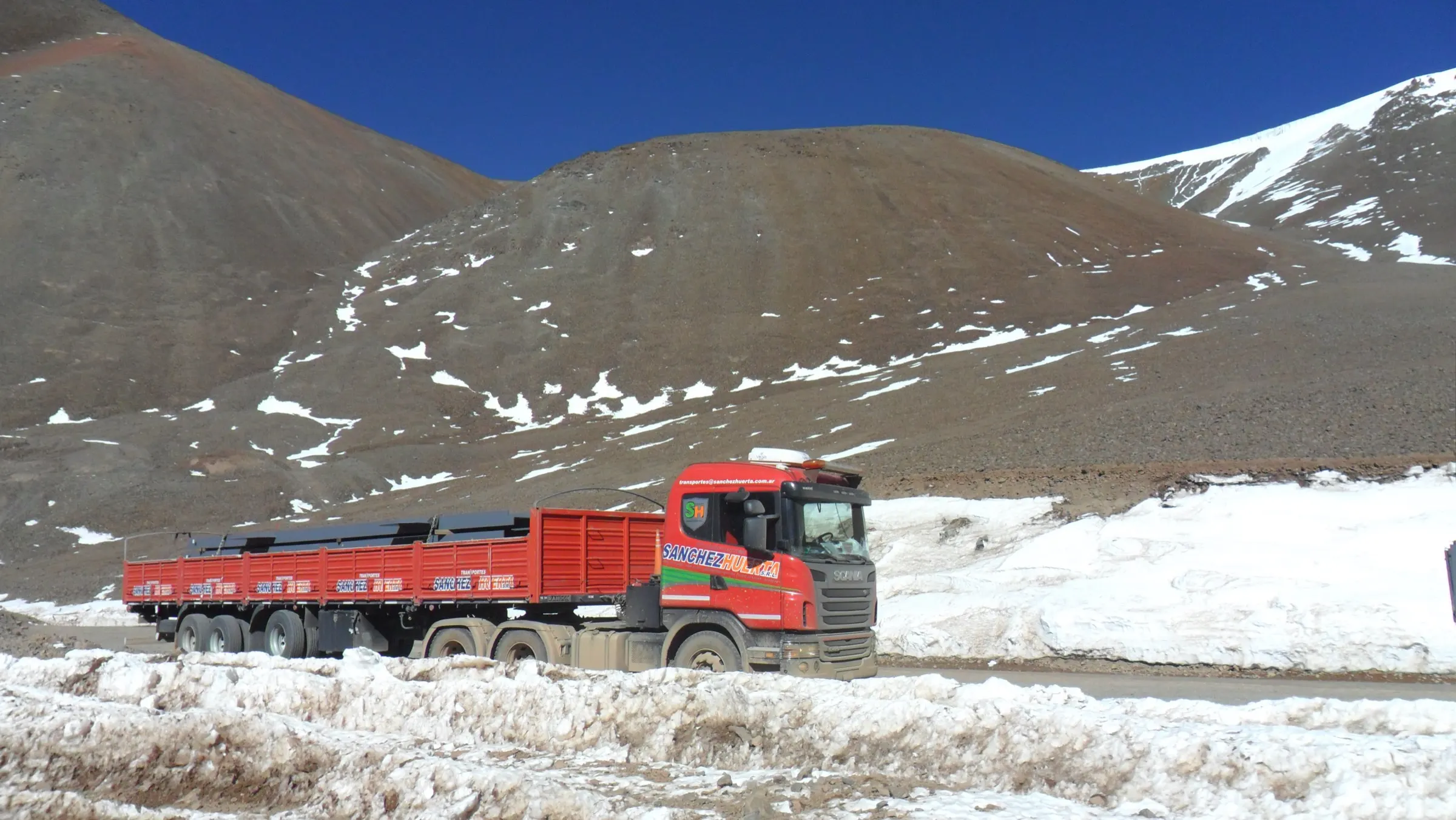 Camión con semirremolque cargado circulando por un paso de alta cordillera con nieve a los costados de la ruta