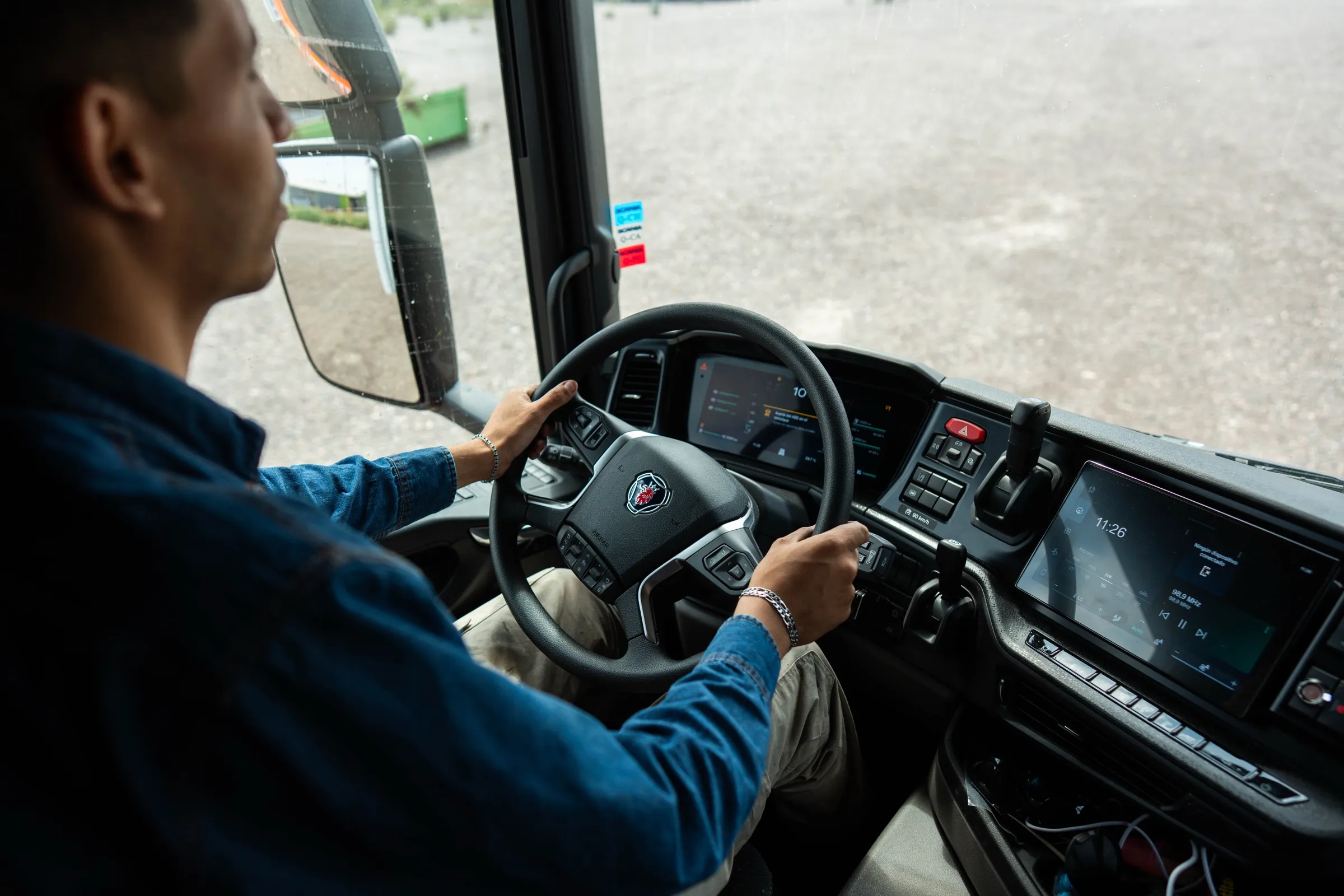 Vista desde el interior de la cabina de un camión Scania, con el conductor sujetando el volante y el tablero digital encendido